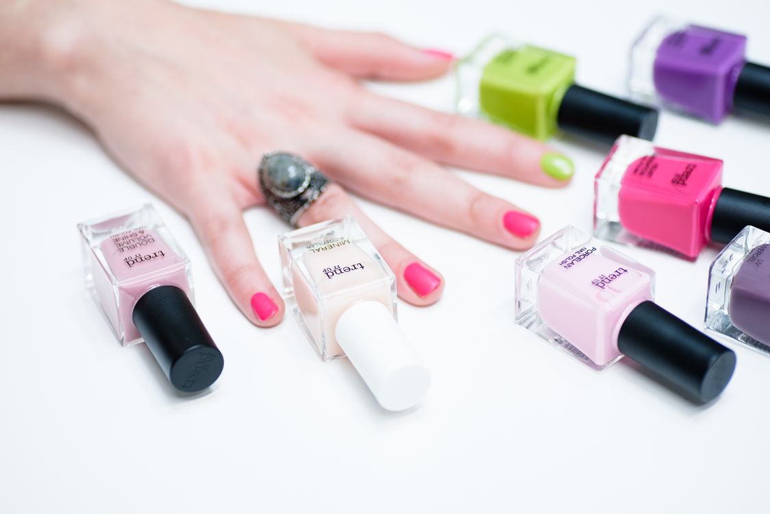 Mano con manicura colorida rodeada de esmaltes